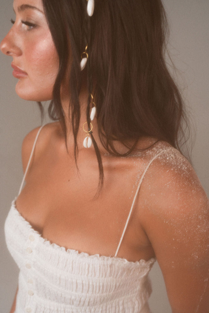 Woman wearing a white top with thin straps and a decorative headpiece against a neutral background